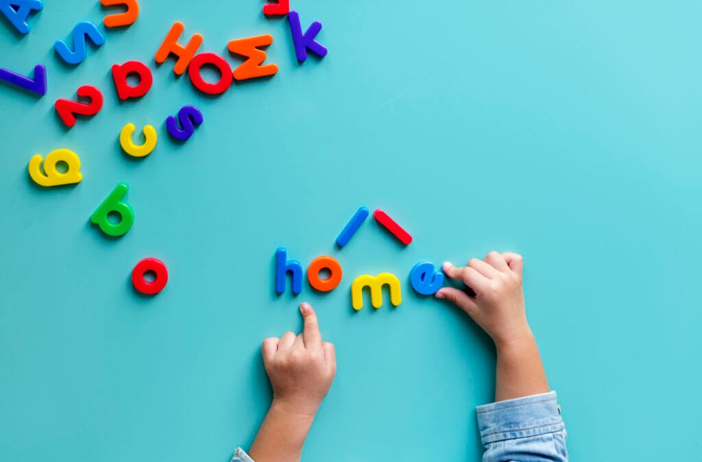 Child plays with plastic letters arranging them into simple words on a blue background