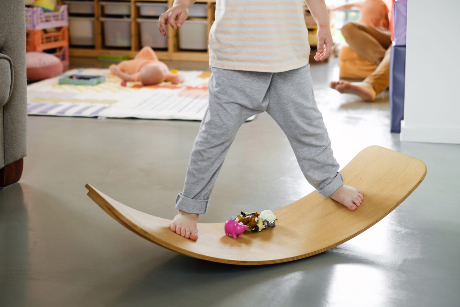 Young boy stands on wooden rocker board in living room, some toys are in the middle of the board. Keeping balance