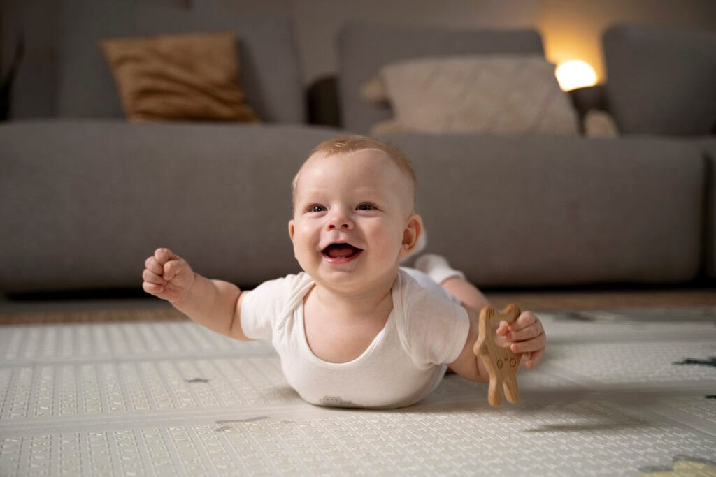 A baby lies on a mat on the floor demonstrating tummy time, holding its head up and with a toy in one hand.